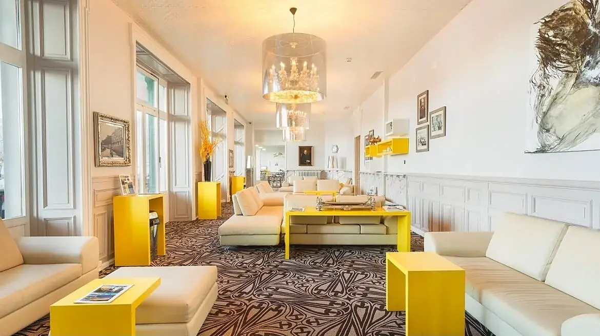 Hình ảnh không gian sảnh chờ sang trọng với ghế sofa trắng, bàn viền vàng và đèn chùm pha lê tại trường quản trị khách sạn César Ritz Thụy Sĩ.